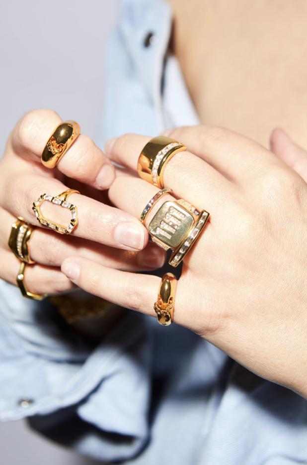 An over-the-shoulder shot of a fashionable woman with gold layered necklaces, flashy rings and dangly earrings.