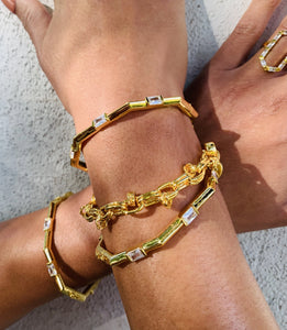 Two gold bracelets on woman's wrist, one with diamonds and one in an intricate design.